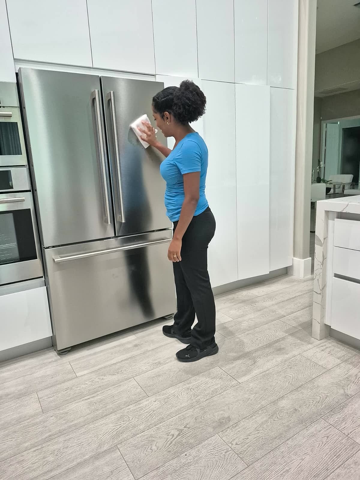 Alessandra cleaning a stainless steel refrigerator in a bright kitchen